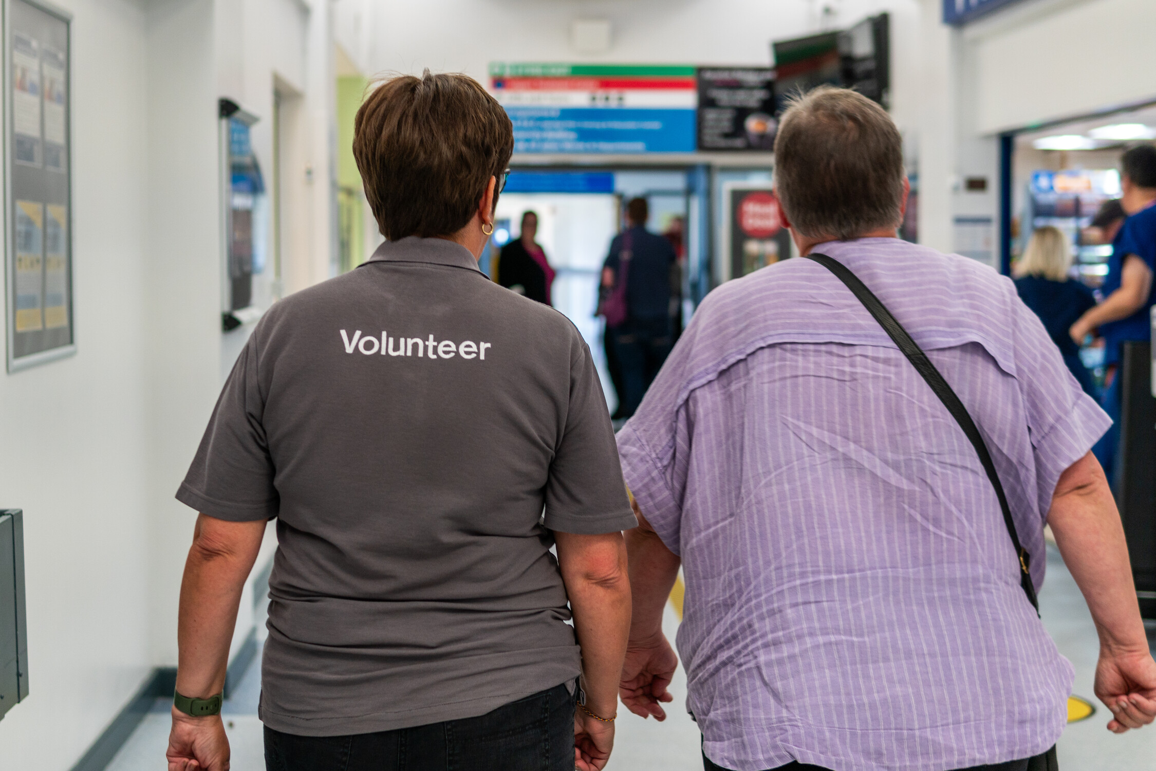 A female volunteer walking alongside a patient in a hospital corridor.