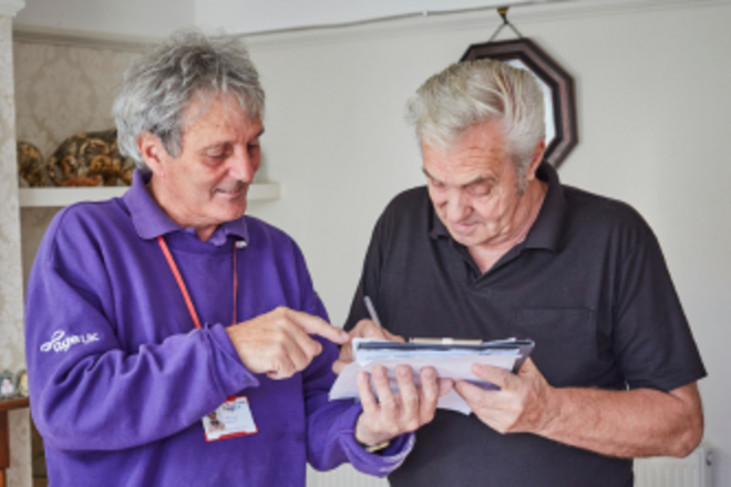 A person showing a man some forms that he is signing in his home.