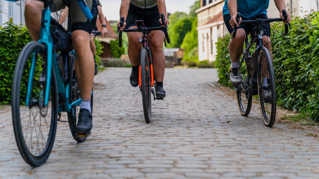 Cycle Three cyclists in a row, cycling down a bush-lined path