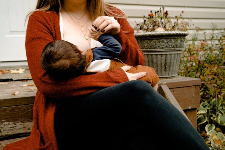 A lady wearing an orange cardigan breast feeds her baby whilst sat on a doorstep.