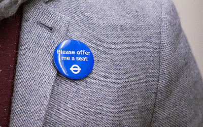 Someone has the 'Please offer me a seat' badge on their grey suit jacket.