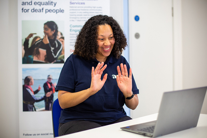 A woman is say in front of a computer doing British Sign Language.