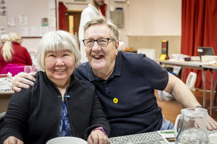 A man and a woman sit next to each other, smiling, at lunch club
