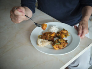 A plate of food on a table. You can see a man holding his fork with a bite of potato on it.